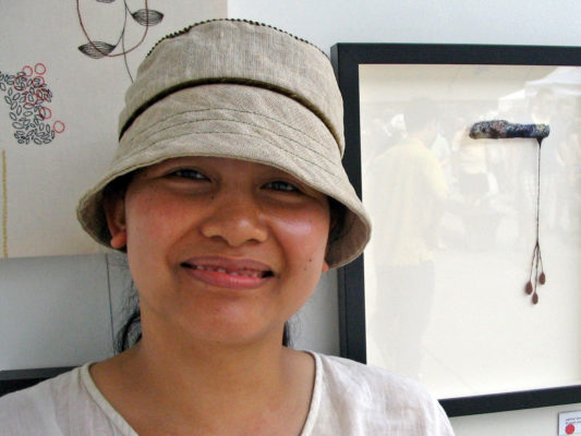 A close up of a woman wearing her new Carval summer hat in front of her artwork at the TOAE