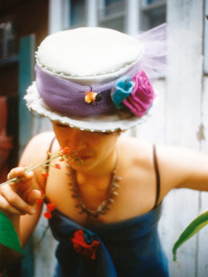 Close up a woman smelling a flower wearing a Bee in the Bonnet hat.