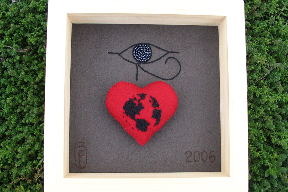 a shadowbox of hand embroidery of Ptah symbol and a felt embroidered heart of the world