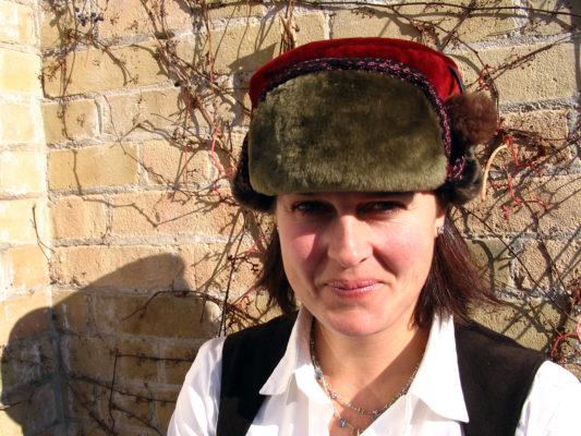 A close up of a woman wearing her new Pom Pom shearling olive green and red hat.