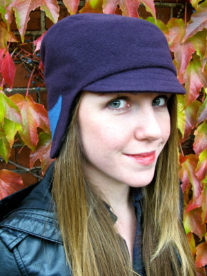 Head shot of a woman wearing the Amelia hat design in dark purple plum colours.