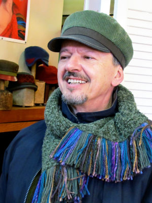 A close up of a man wearing a Cordy Cap in sage green and brown colours with a sage green boucle knit scarf