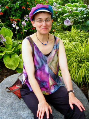A woman wearing her new Delbert cap sitting down in a garden.