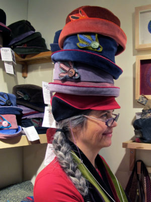 Gwendolyne wearing 4 hats stacked on top of one another at the One of a Kind show