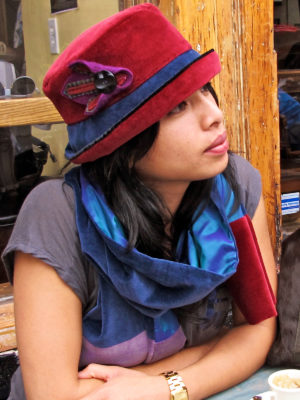 A close up of woman wearing a red and blue Labijou Hat sitting infant of a cafe in the Fall.