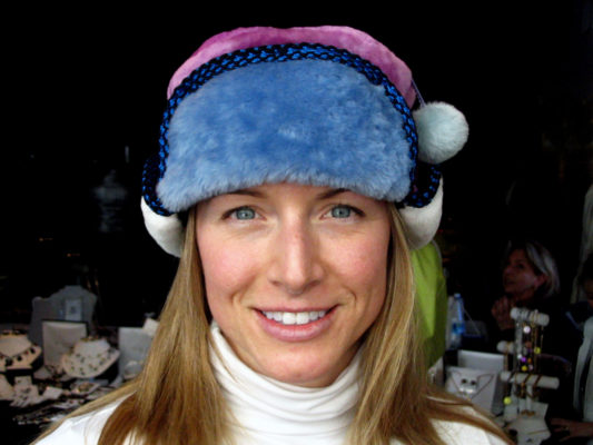 A close up of a woman wearing a light blue, hot pink and white Pom Pom Hat