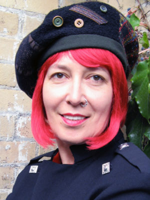 A close up of a red headed woman wearing a black and olive Celeste Beret hat outside