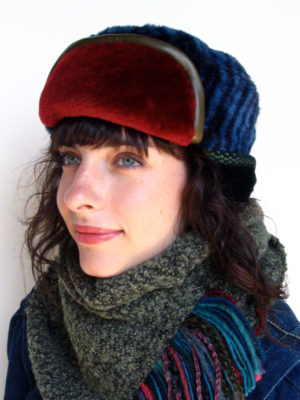 A close up of woman wearing a dark blue stripe and red Snowflake shearling fur hat.