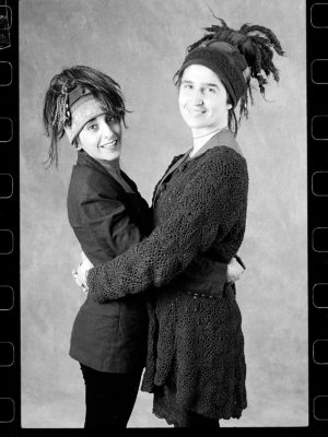 An early black and white photo of two friends modelling Gwendolyne Hats wool Twirl String Toque.