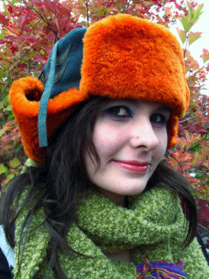 A close up of a orange and green Winter Wave hat on a woman outside in the Fall.