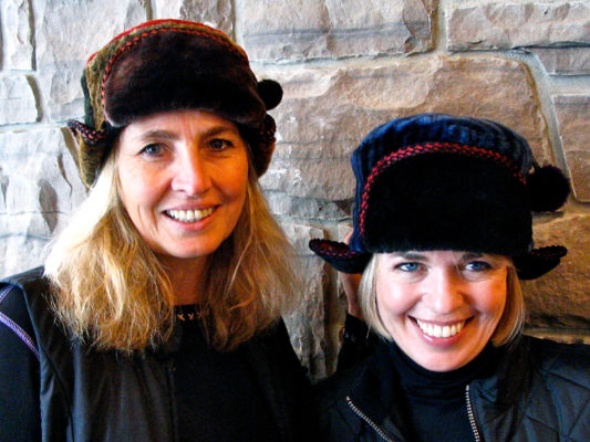 Close up of 2 women wearing a brown and blue Pom Pom hats