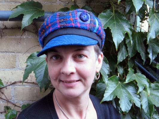Close up of a woman wearing a royal blue Abbey Road cap outside in front of a wall of ivy