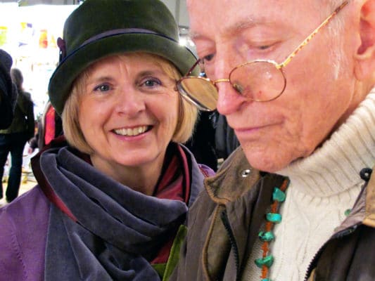 Woman wearing her LaBijou olive hat with a velvet silk scarf on behind her husband